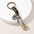 Detail of vintage bronze keychain with braided leather, engraved charms, and guitar pendant - Guitar