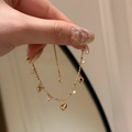 Dettaglio di un bracciale dorato con ciondoli a cuore e zirconi indossato al polso - Bracciale Oro