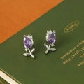 Primer plano de pendientes de tulipa en plata con circón morado sobre libro verde - Blanco K + Púrpura