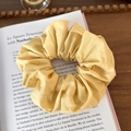 Detail of yellow fabric scrunchie with pleated texture placed on an open book - Yellow