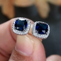 Macro shot of square-cut sapphire blue stud earrings with white zircon halo detailing - Blue