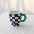 Irregular blue and white checkered ceramic mug with green handle and wavy rim edge - Blue Checkerboard Cup