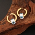 Gold evil eye hoop earrings with blue bead on a rustic wooden background - White