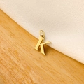 Macro shot of a golden letter K pendant on a white satin and light wood surface - 14k Letter - K (letter Height 1cm)