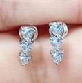 Three-heart silver drop earrings with cubic zirconia stones held between fingers - Platinum White Zircon