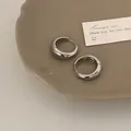 Dettaglio di orecchini a cerchio in argento lucido su un vassoio di ceramica beige - Argento 26mm (Grande)