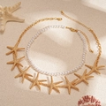 Detail von Strand-Perlen-Choker und Goldstern-Halskette auf sandigem Hintergrund - Goldener Seestern (2-teiliges Set)