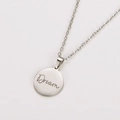 Macro view of silver stainless steel round pendant with engraved Dream script text - Steel