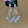 Makro-Detail goldener Quastenohrringe mit funkelnden Strasssteinen und tropfenförmigen Kristallen - Silberohrstecker - Goldfarben - Weißer Zirkon