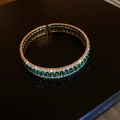 Makroaufnahme eines goldenen Armreifs mit smaragdgrünen und weißen Zirkonia-Steinen - Cuff Bracelet / Gold Grüner Rechteckiger Zirkon