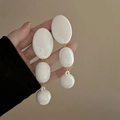 White acrylic oval tassel drop earrings with gold links shown held against beige wall - Silver Earring Post-White