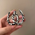 Orecchini a cerchio placcati oro con motivo a cuore nero e bianco tenuti in mano - Perno in Argento S925 Pelle Ovale Bianco e Nero