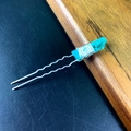 Macro detail of U-shaped hair pin with light blue crystals on textured wood surface - Teal