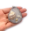 Pendente a goccia con tre conchiglie naturali e bordo in strass tenuto in mano - Bianco