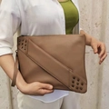 Brown rivet punk clutch with diagonal stitching and wrist strap held by model - Camel