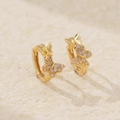 Elegant gold butterfly huggie earrings with sparkling crystals on a textured background - Gold