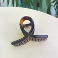 Gros plan d'une pince à cheveux ambre en résine avec un design torsadé élégant - Moyen / Écaille Claire Brillante
