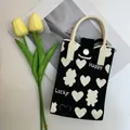 Detail of knitted phone bag with heart pattern and Happy Lucky woven text - Heart Black-Happy/Lucky
