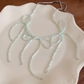 Light green beaded bow necklace with elegant tassels on a cream-colored plate - Green Beaded