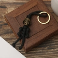 Handmade black paracord keychain with bronze skull bead and gold ring on wooden base - Black
