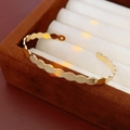 Detalle de un brazalete dorado con bordes ondulados colocado en un estuche de terciopelo - Elipse / Dorado