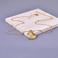 Detail of a 18K gold stainless steel necklace with a shell pendant on a marble stand - Shell