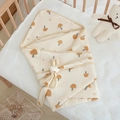 Detail of mushroom print cotton muslin swaddle blanket folded on a wooden baby crib - 90*90cm / Brown Mushroom