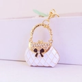 Macro shot of white quilted handbag keychain with gold trim and rhinestone bow accent - White
