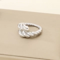 Macro shot of silver croissant ring with twisted rope design on a textured display base - US 6