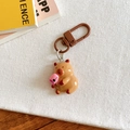 Detailed close-up of a brown capybara keychain holding a pink drink on white fabric - Drinking Beverage Style