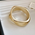 Detalle macro del brazalete de onda dorada pulida con textura metálica orgánica - Estilo Espiral / Dorado