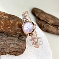 Macro detail of gold-tone watch band with pink gemstones and gradient dial face - Pink