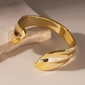 Detailaufnahme eines polierten goldfarbenen Armreifens auf einem Naturstein-Hintergrund - Gold