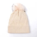Close-up of cream knit beanie with thick ribbed texture and fluffy faux fur pom-pom - Geometric Knit Beanie / Beige