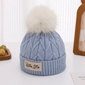 Detail von Baby-Strickmütze mit weißem Kunstfell-Bommel und Markenetikett - Ca. 2-5 Jahre alt / Blau