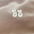 Macro shot of white heart-shaped acrylic earring backs on soft pearlescent fabric - White