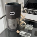 Detail of dark grey mesh bag with cartoon eyes on a desk with lifestyle accessories - Gray