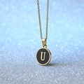 Golden necklace with circular black enamel pendant featuring a gold letter U design - Letter U