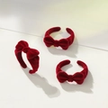 Tres anillos de lazo en terciopelo rojo oscuro presentados sobre una revista con estilo elegante - Anillo de Fresa