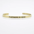Golden stainless steel cuff bracelet engraved with Partners In Wine decorative text - PARTNERS IN WINE