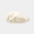 Detailed macro view of beige wool beret featuring a silver metal logo and soft fabric texture - White