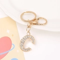 Golden keychain with rhinestone-encrusted letter C pendant on a white ceramic plate - Letter C