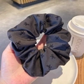 Chouchou en tissu gris foncé à motifs nœuds mignons tenu à la main dans un café cosy - Petit imprimé nœud / Noir