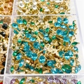 Goldene Blumenanhänger mit türkisfarbenen Steinen in einem transparenten Sortierkasten - See Blau