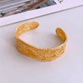Macro detail of gold-plated open cuff bracelet featuring vintage relief pattern and texture - Gold