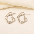 Dettaglio degli orecchini a forma di G in acciaio inossidabile 304 su tessuto beige - Stile Forma Onda Organica Fusa (D219-S) / Argento