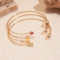Detail van drie gouden armbanden met veelkleurige zirkoon in hart- en druppelvorm - Armband - Goud - Gekleurde Zirkonia (3-delige set)