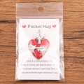 Red Pocket Hug heart charm with silver metal cross and inspirational gift card on wood - Thorns Cross Red Heart