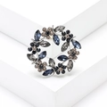 Elegant silver-tone wreath brooch with navy and dark grey crystals on white pedestal - Gray