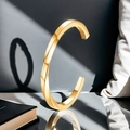 Vista macro del bracciale ritorto dorato con finitura lucida e design geometrico a forma di C - Oro